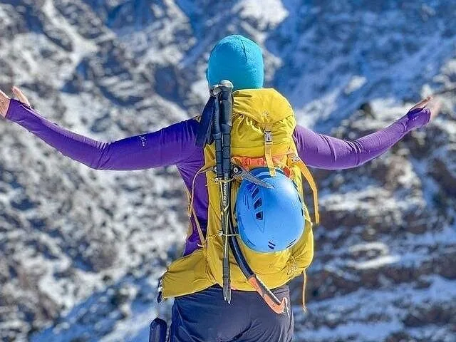 Randonneur les bras tendus vers des montagnes enneigées, portant un sac à dos jaune